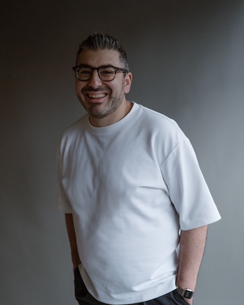 Serop Yildiz, lachend, in een wit T-shirt voor een donkere wand